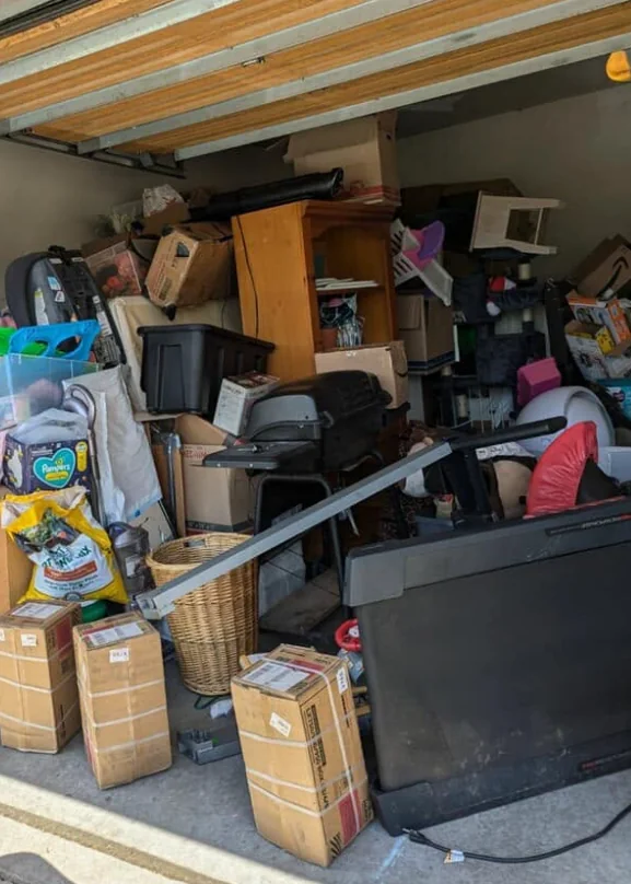 Space behind a roll-up door packed with boxes, a bookcase, a grill and a treadmill